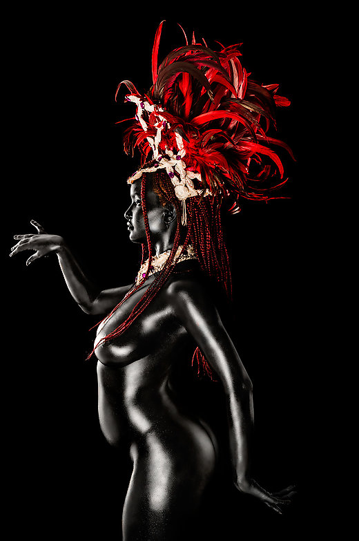 A woman, body-painted in black wearing a red feather and bejewelled headdress.